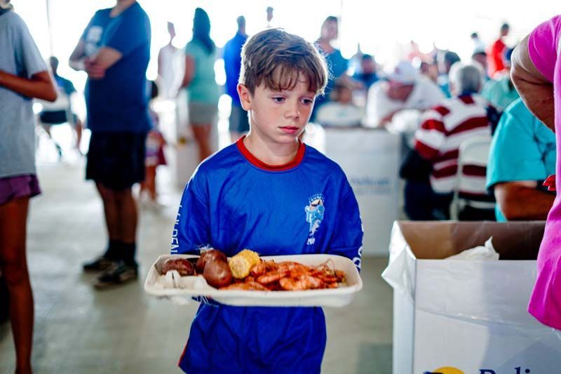 A young boy in a blue shirt is holding a tray of food.
