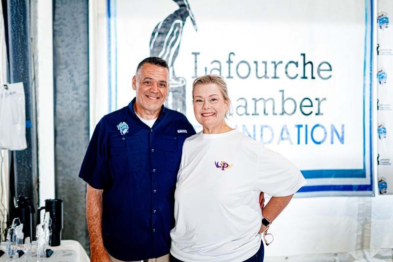 A man and a woman are posing for a picture in front of a lafourche amber foundation sign.