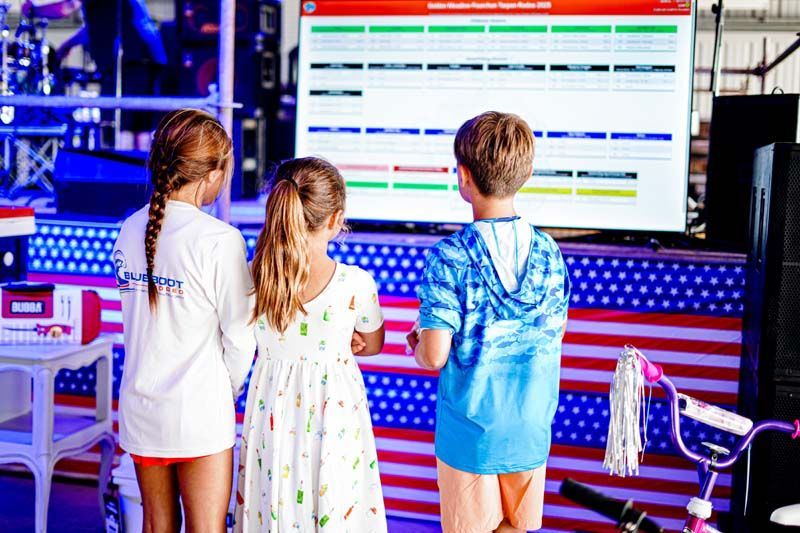 Three children are standing in front of a large screen.