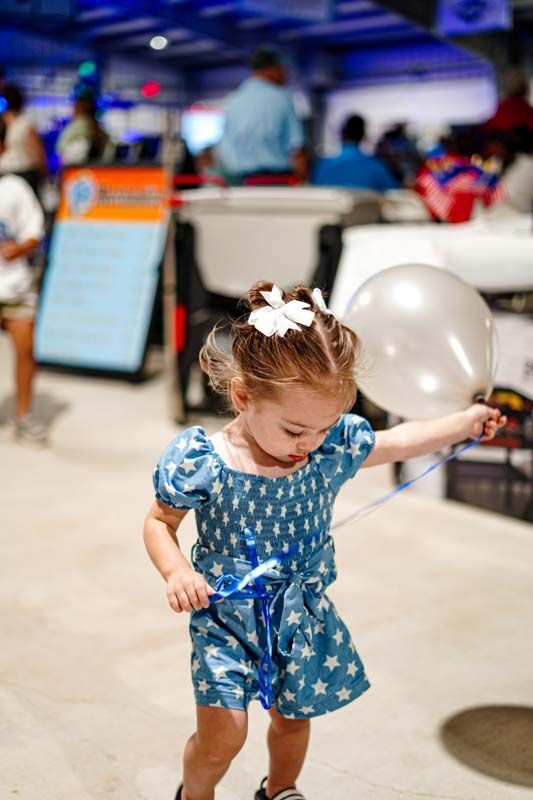 A little girl is holding a balloon in a bowling alley.