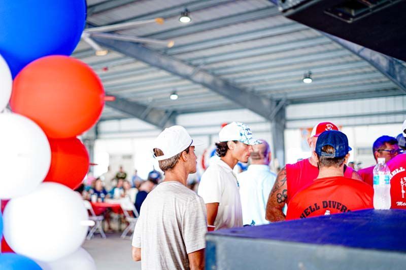A group of people are standing in a room with red , white and blue balloons.