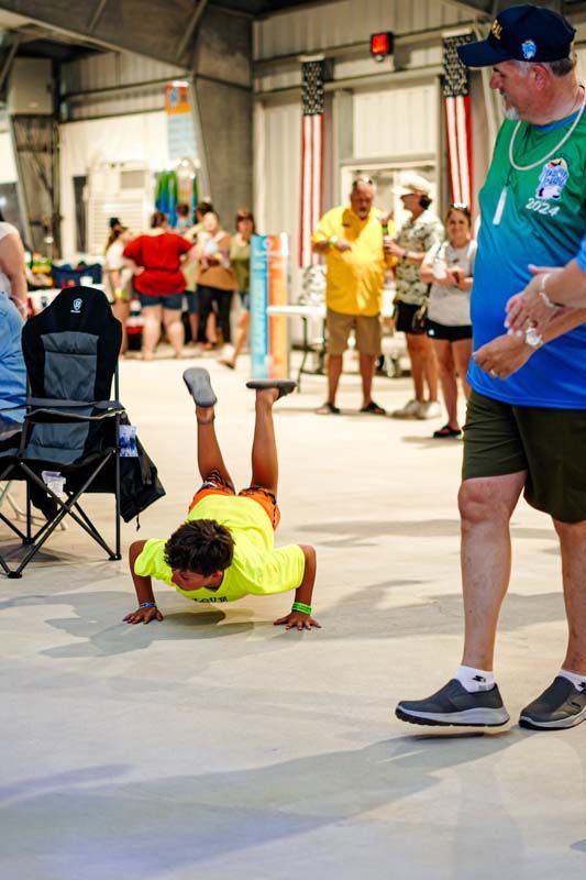 A man is standing next to a boy doing a handstand on the floor.
