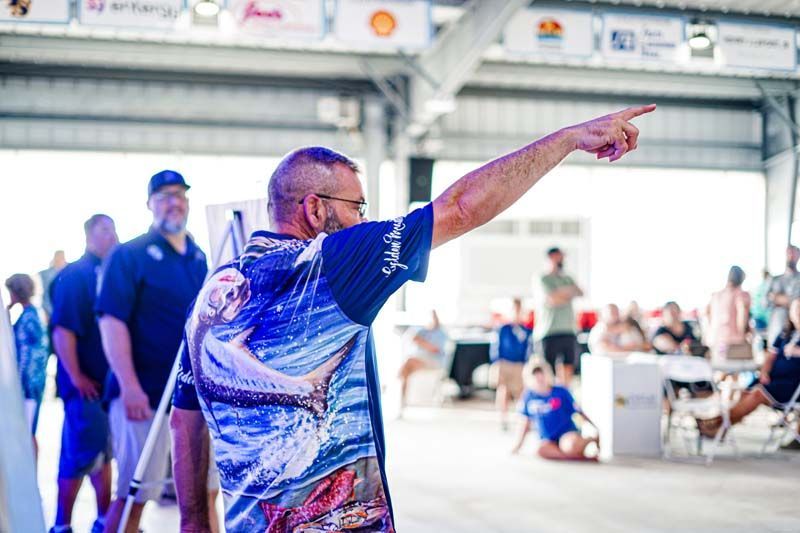 A man in a blue shirt with a fish on it is pointing at something.