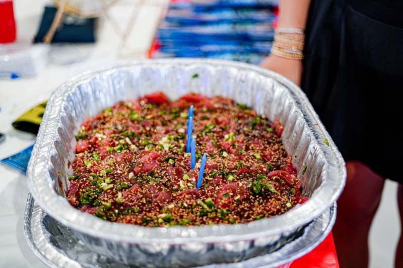 A person is holding a pan of food with a blue candle in it.