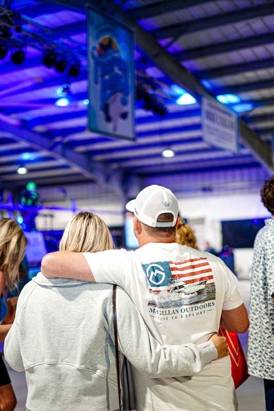 A man in a white shirt with an american flag on the back is hugging a woman.