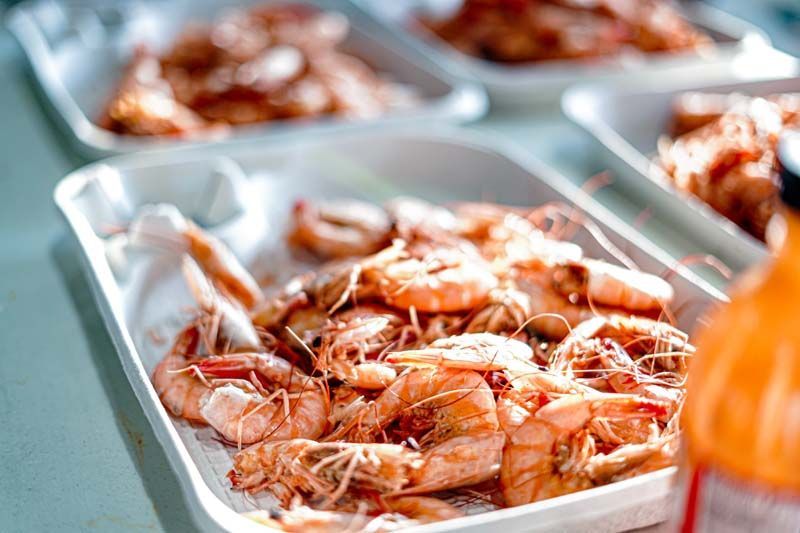 A tray of shrimp is sitting on a table next to a bottle of soda.