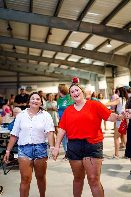 Two women are standing next to each other in a room holding hands.