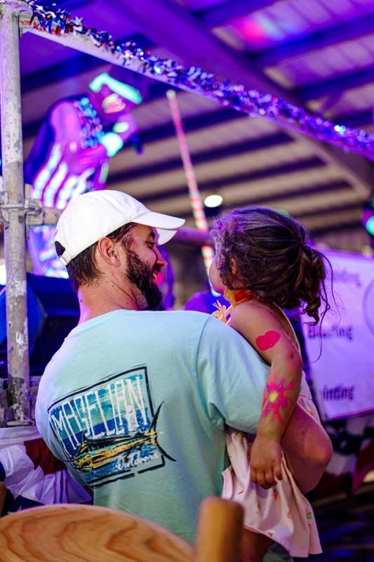 A man is holding a little girl in his arms at a carnival.