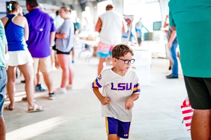 A young boy wearing a lsu jersey is standing in a crowd of people.