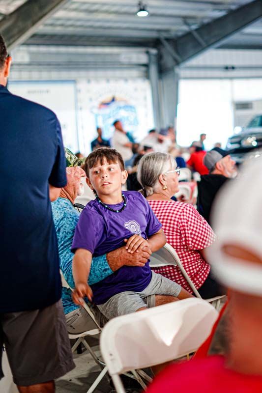 A young boy is sitting in a chair in a crowd of people.