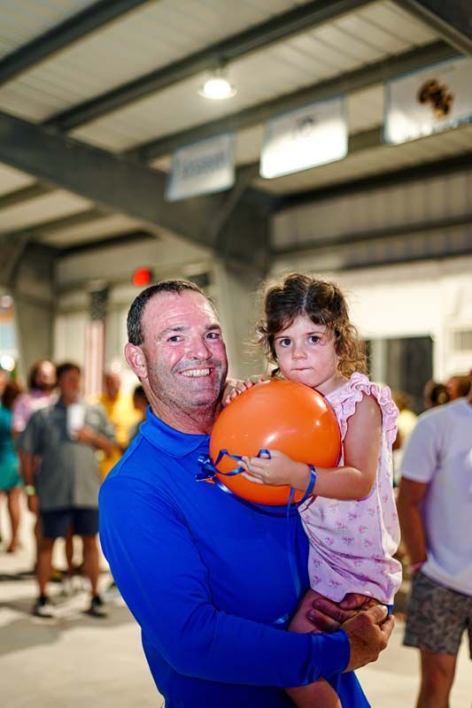A man is holding a little girl who is holding an orange balloon.