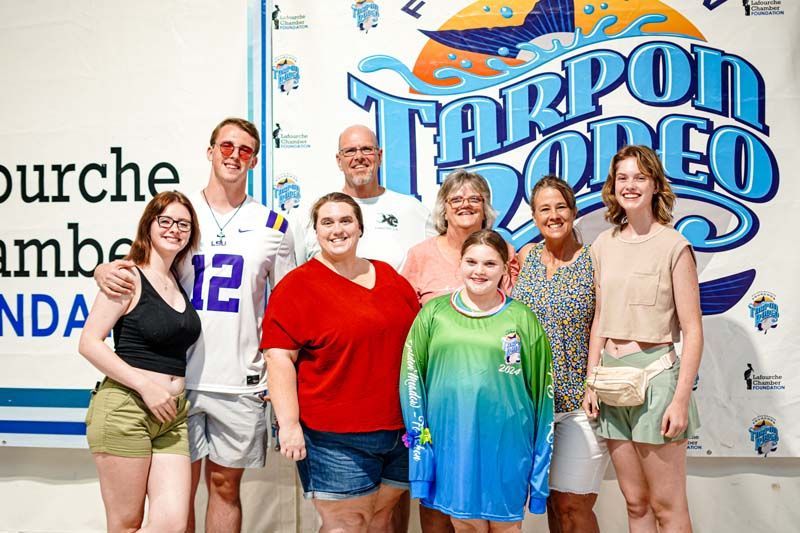 A group of people are posing for a picture in front of a tarpon rodeo sign.