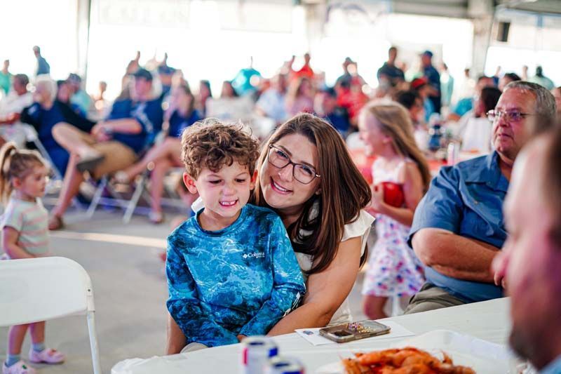 A woman and a child are sitting at a table in front of a crowd of people.