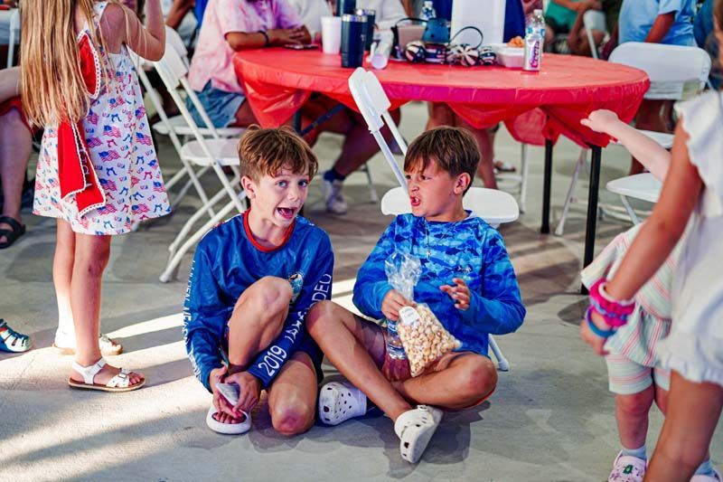 Two young boys are sitting on the ground eating popcorn.