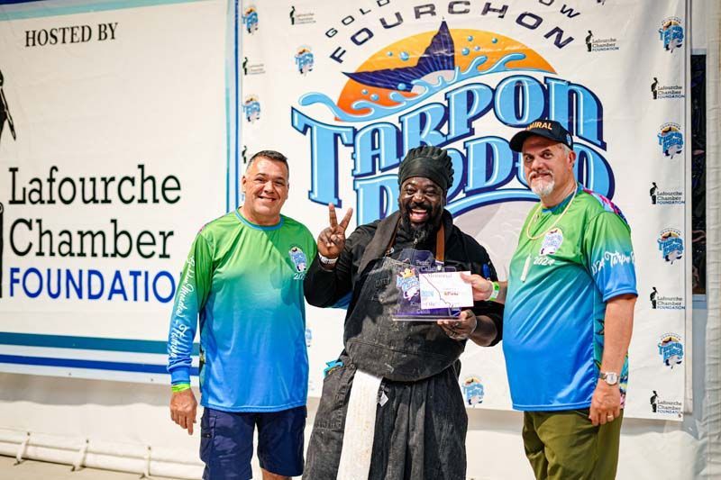 Three men are posing for a picture in front of a tarpon noodle sign.
