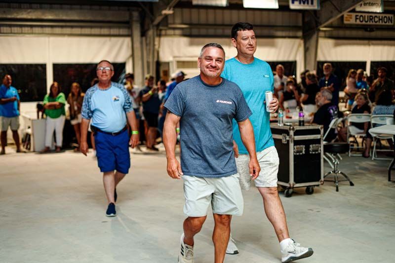 Two men are walking in a room with a crowd of people.