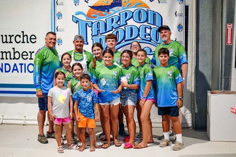 A group of people are posing for a picture in front of a tarpon rodeo banner.