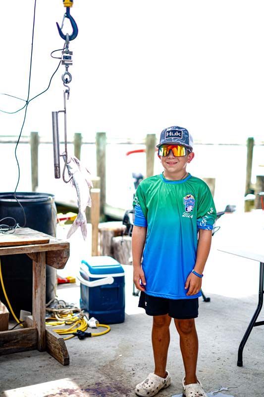 A young boy wearing sunglasses and a hat is standing in front of a table.