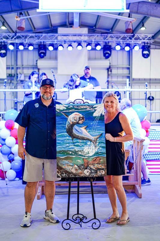 A man and a woman are standing next to a painting of a fish on an easel.