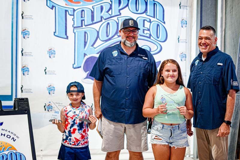 A group of people standing next to each other in front of a tarpon rodeo sign.