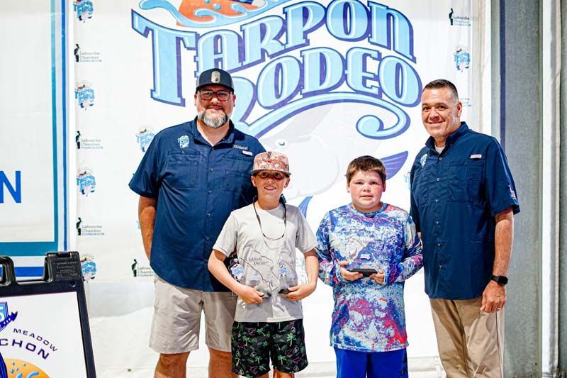A group of people standing in front of a tarpon rodeo sign.