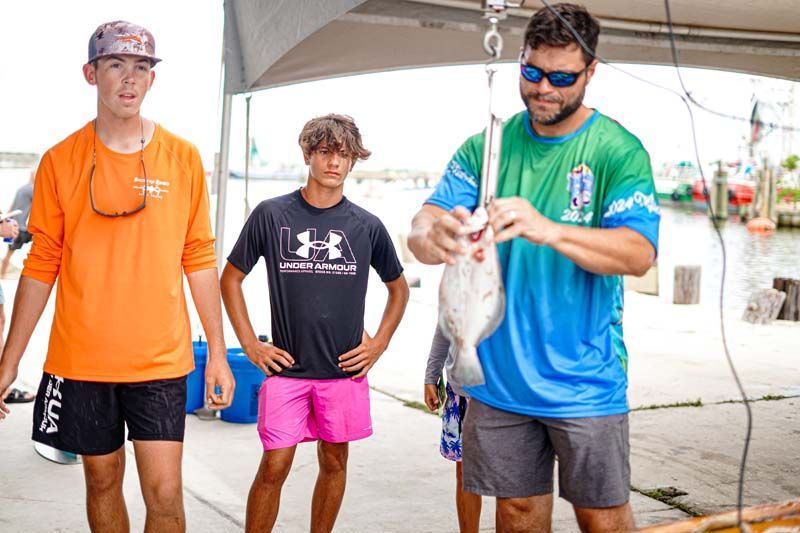 A man is holding a fish on a hook while two other men look on.