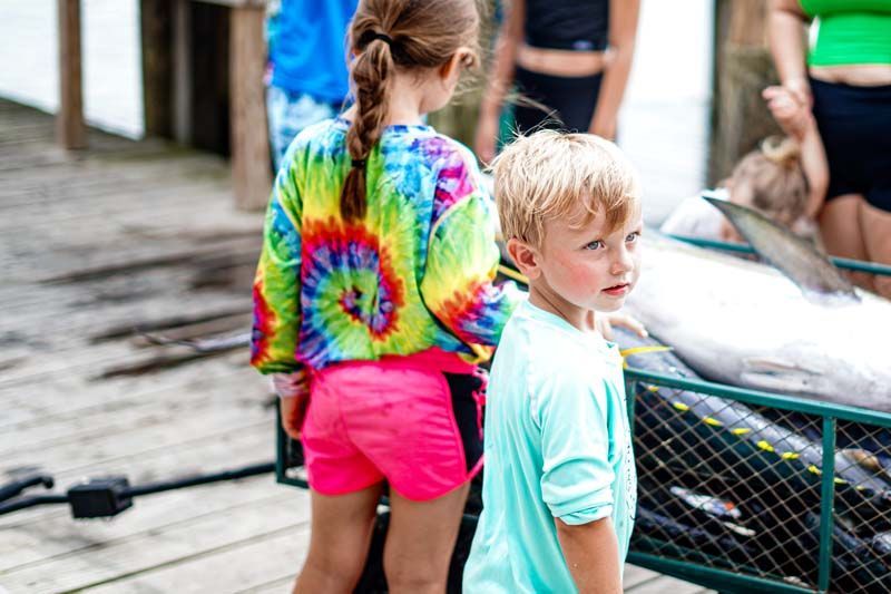 A boy and a girl are standing next to a cart full of fish.