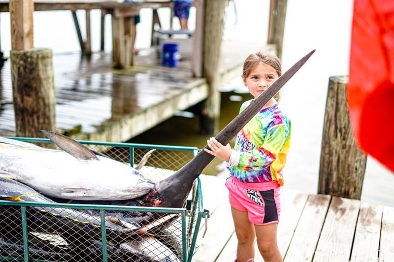 Little girl in tie-dye shirt holds the nose of a swordfish.
