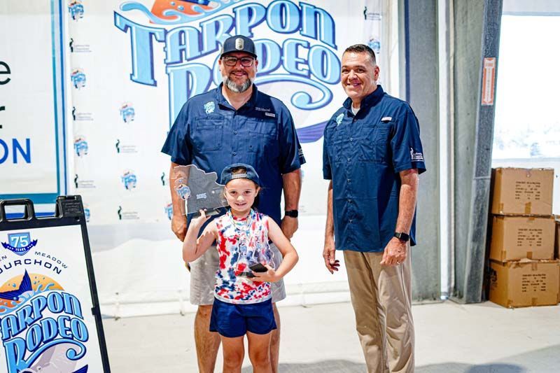 Two men and a little girl are standing next to each other in front of a sign.