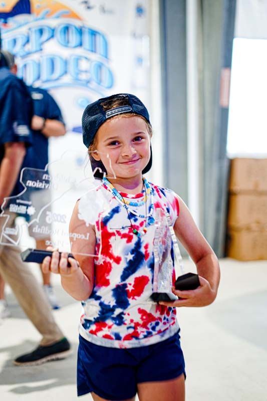 A little girl is holding a trophy and a cell phone.