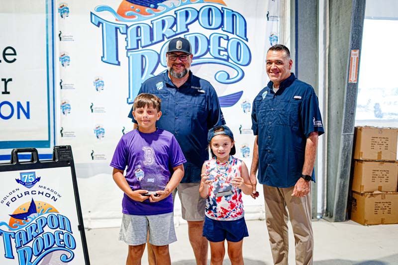 A group of people standing next to each other in front of a tarpon rodeo sign.