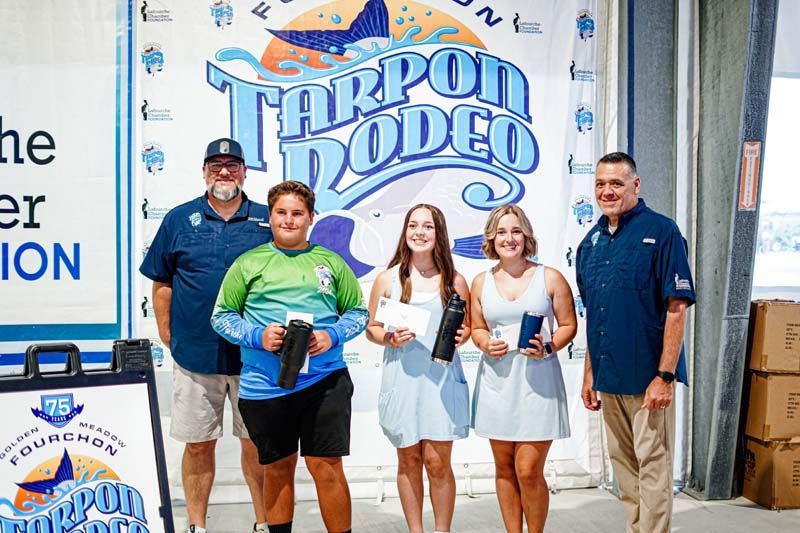 A group of people standing in front of a tarpon rodeo sign.