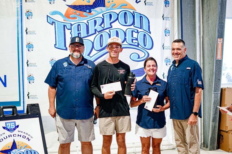 A group of people standing next to each other in front of a tarpon rodeo sign.
