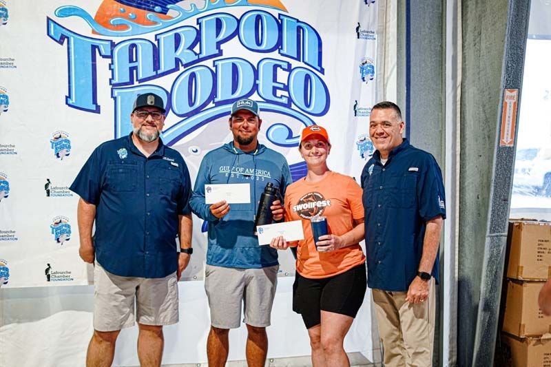 A group of people standing next to each other in front of a tarpon rodeo sign.