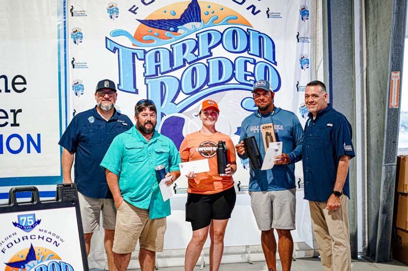 A group of people are posing for a picture in front of a tarpon rodeo banner.