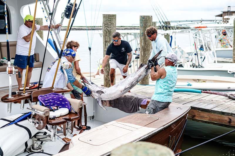 A group of people are standing around a boat holding a large fish.