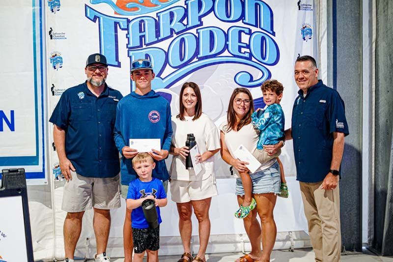 A group of people standing in front of a tarpon rodeo sign.