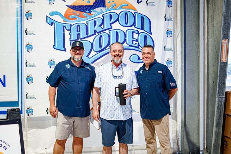 Three men are standing in front of a tarpon rodeo sign.