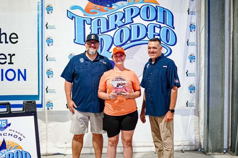 Three people are standing next to each other in front of a tarpon rodeo sign.