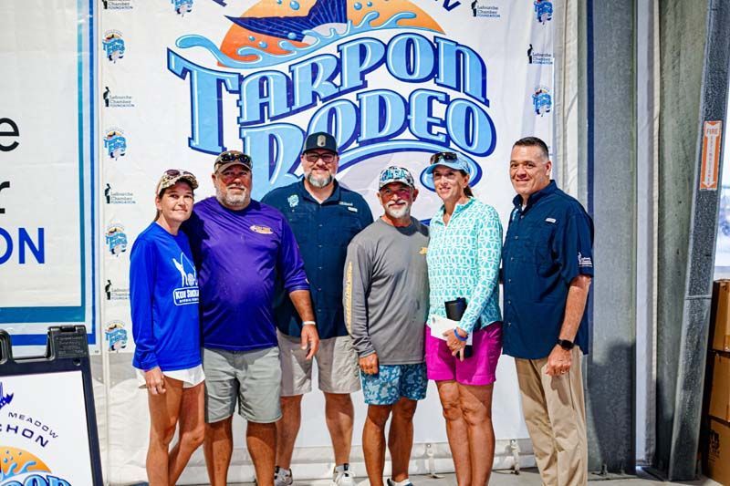 A group of people are posing for a picture in front of a tarpon rodeo sign.
