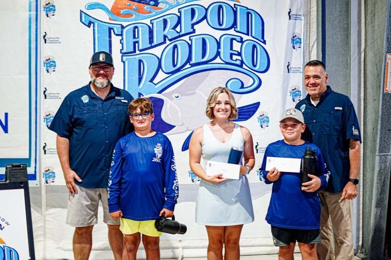 A group of people standing in front of a tarpon rodeo sign.