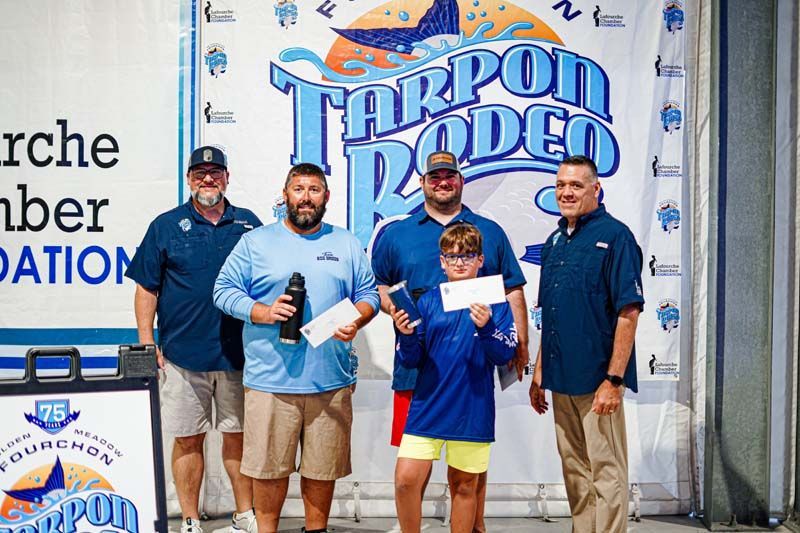A group of men are standing in front of a tarpon rodeo sign.