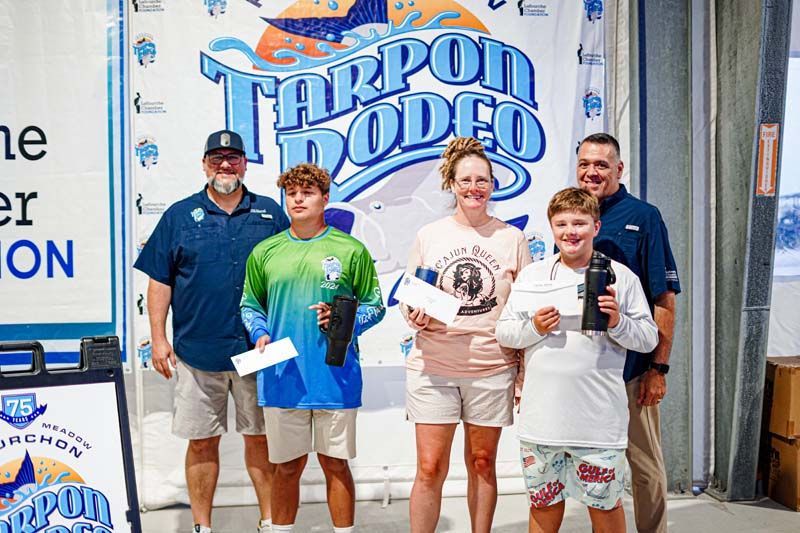A group of people standing in front of a tarpon rodeo sign.