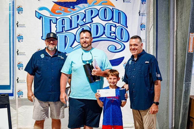 A group of men are standing next to each other in front of a tarpon rodeo sign.