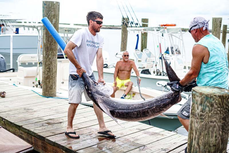 A man is carrying a large fish on a dock.