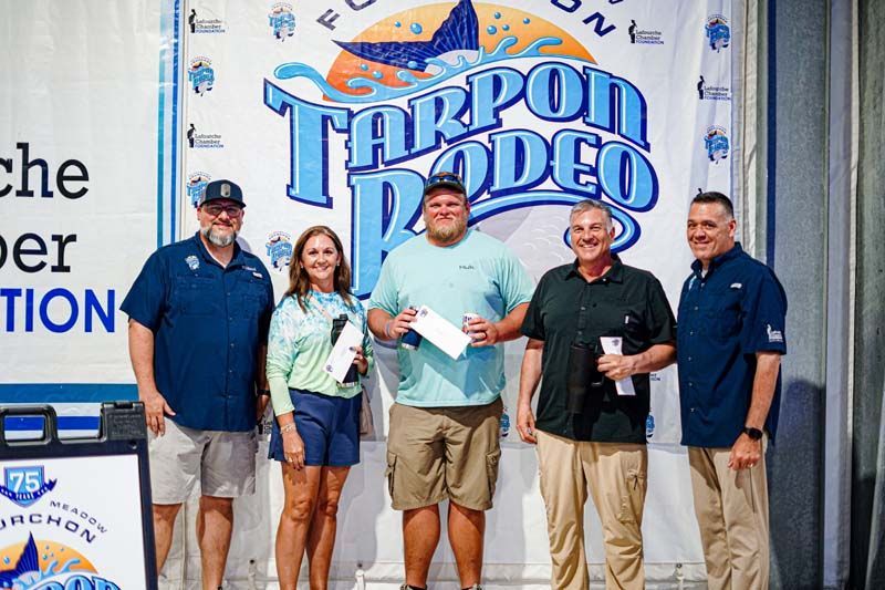 A group of people standing in front of a tarpon rodeo sign.