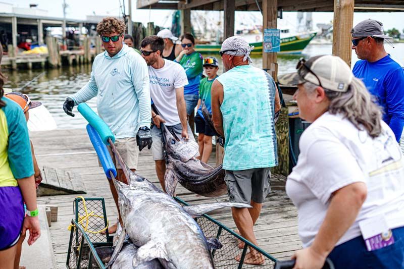 A group of people are standing around a large fish on a dock.