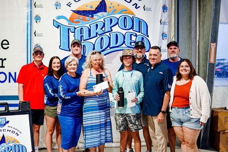 A group of people are posing for a picture in front of a sign that says tarpon rodeo.