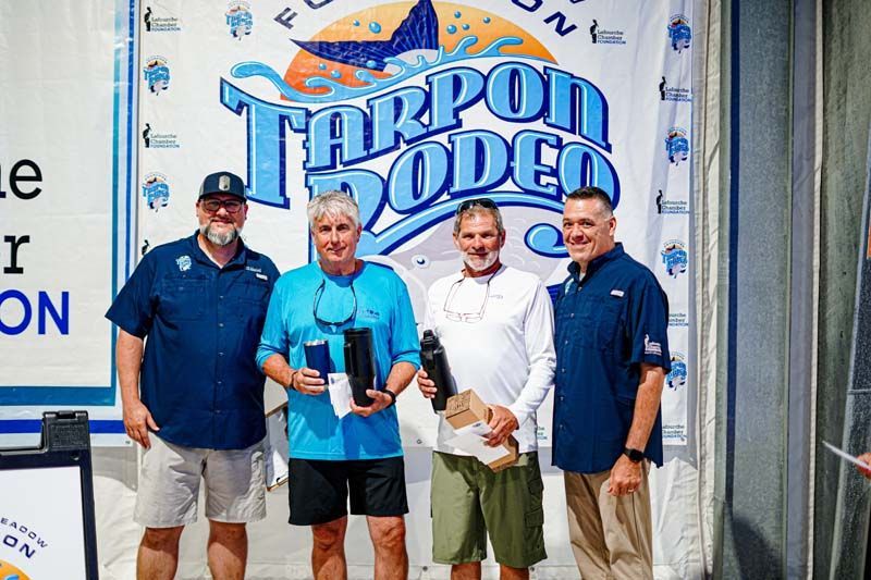 A group of men are standing in front of a tarpon rodeo sign.