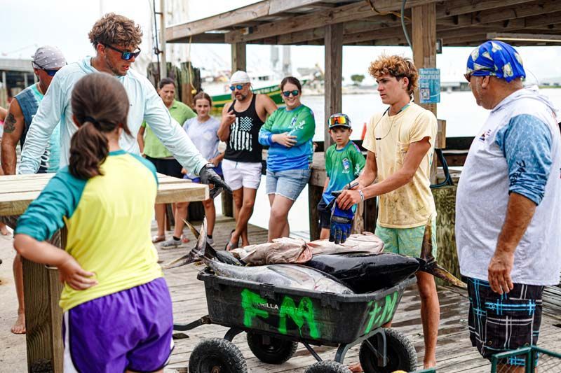 A group of people are standing around a cart filled with fish.
